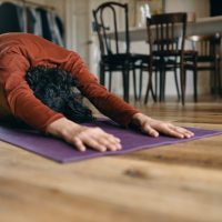 Unrecognizable man with black hair doing yoga at home, having rest in balasana or child pose, relaxing body muscles between asanas, stretching lower back and hips. Relaxation and health concept